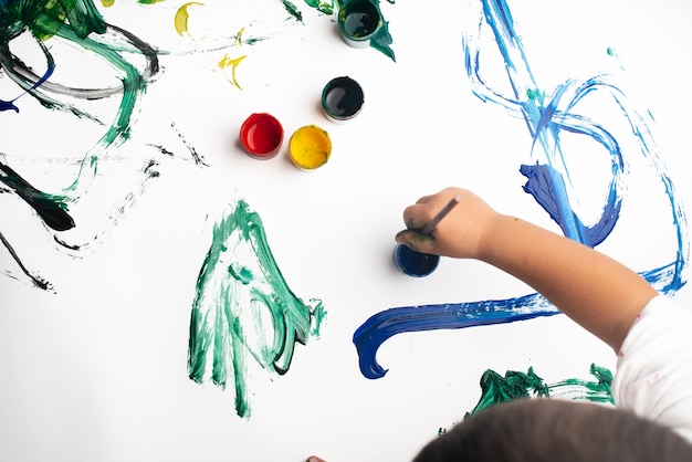 Mains d'un petit garçon en train de peindre à l'aquarelle sur une feuille de papier blanc.