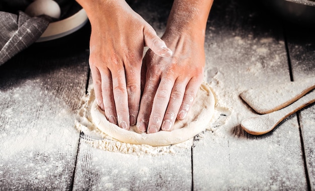 Mains pétrissant une pâte pour la cuisson des pizzas avec de la farine