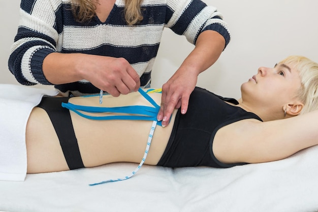 Les mains d'une physiothérapeute féminine appliquent un ruban thérapeutique élastique adhésif sur l'abdomen féminin