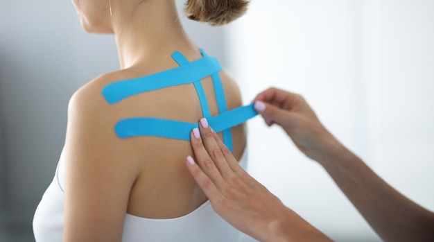 Les mains des physiothérapeutes collent un ruban adhésif bleu sur le dos d'une jeune patiente en gros plan.