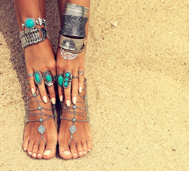 Les mains et les pieds bronzés de la femme avec une manucure et une pédicure blanches soignées décorées par des bracelets et des bagues en argent de style Boho Détente sur la plage tropicale
