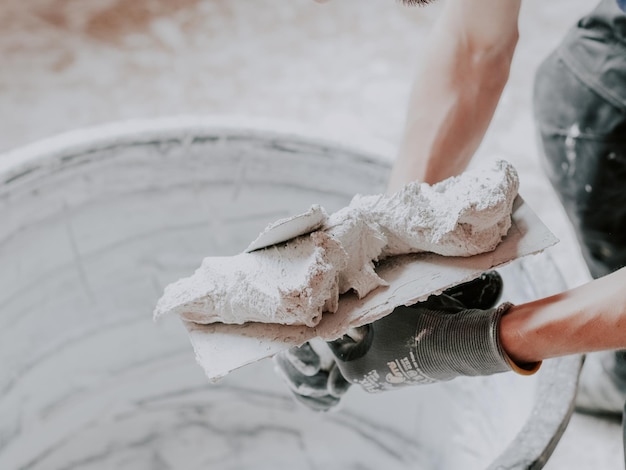 Les mains d'un plâtrier caucasien j'applique du mastic frais avec une spatule à l'autre