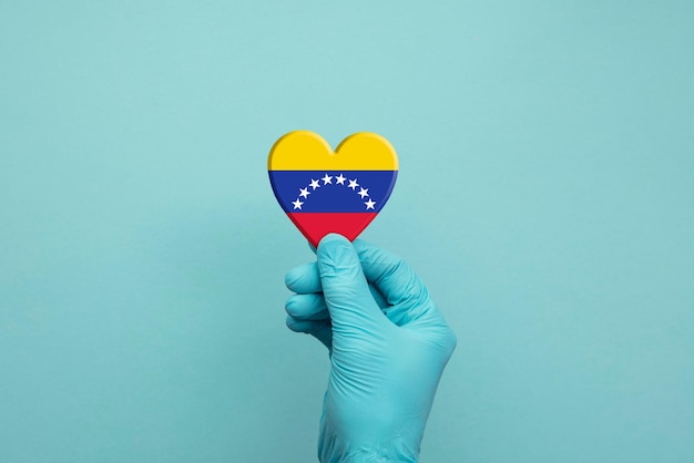 Mains portant des gants chirurgicaux de protection tenant le coeur du drapeau du venezuela