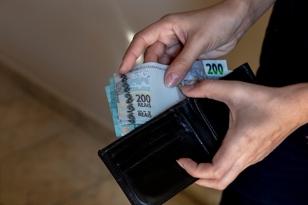 Mains avec portefeuille noir mettant de l'argent brésilien.