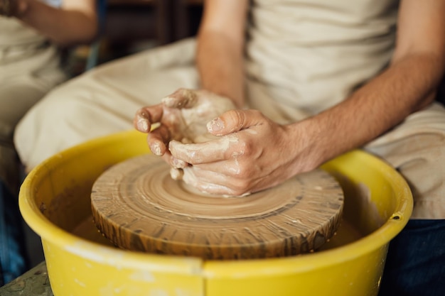 Mains d'un potier fabriquant un pot en céramique sur le tour de potier