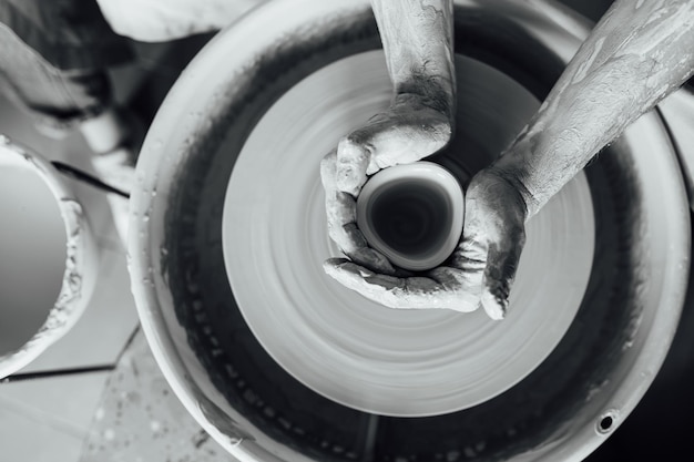 Mains d'un potier fabriquant un pot en céramique sur le tour de potier