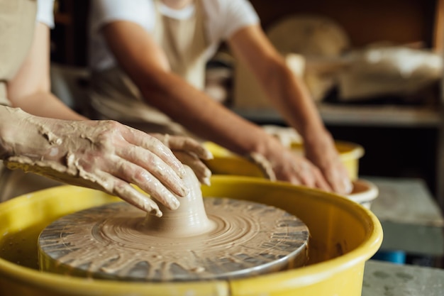 Mains d'un potier fabriquant un pot en céramique sur le tour de potier