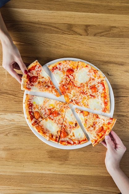 Mains prenant la pizza de l'assiette