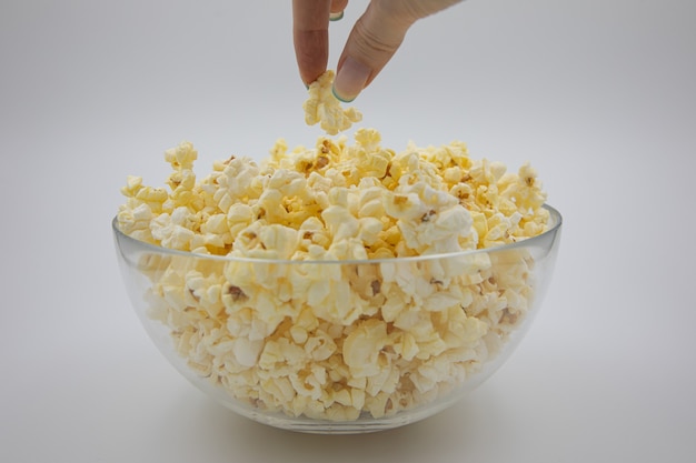 les mains prennent du pop-corn dans une assiette en verre