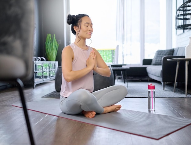 Mains de prière yoga et méditation d'une femme asiatique dans le salon de la maison pour l'exercice de pleine conscience Zen chakra pilates et yogi féminin s'entraînant et méditant avec la pose de la main namaste pour la détente et la paix