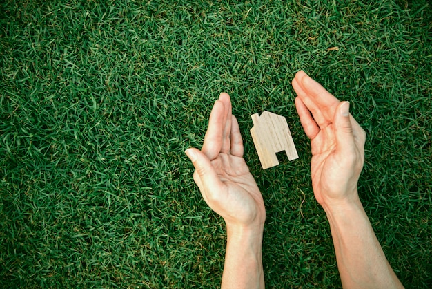 Les mains protègent la maison en bois sur l'herbe verte