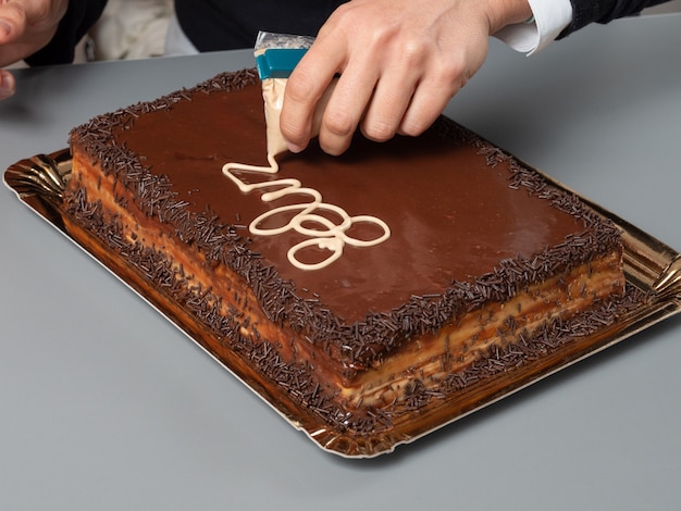 Les mains en pull noir écrit avec un liquide blanc sur un gâteau brun avec des copeaux de chocolat