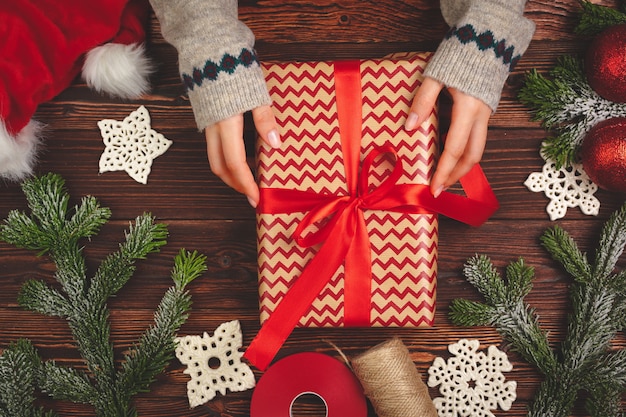 Mains en pull tenant un cadeau sur une table en bois avec des décorations de Noël