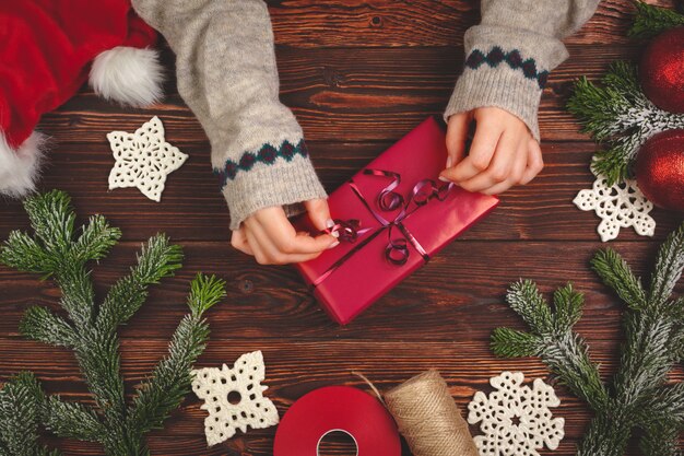 Mains en pull tenant un cadeau sur une table en bois avec des décorations de Noël