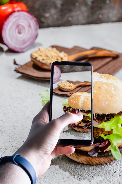 Photo mains ramassant un smartphone en prenant une photo d'un hamburger. espace pour le texte. mise au point sélective