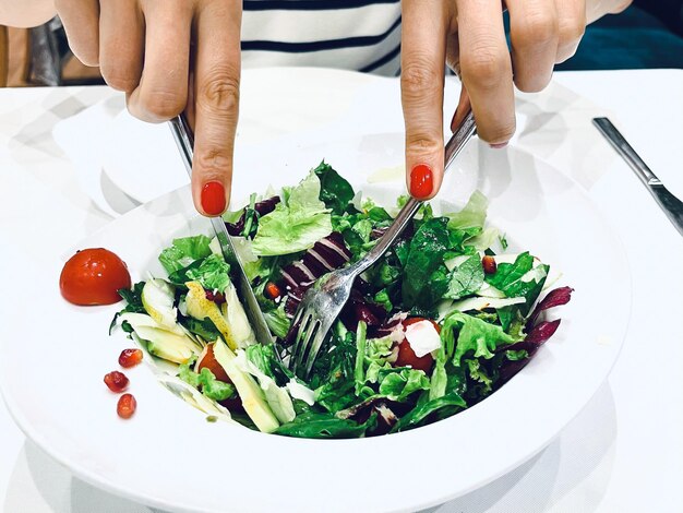 Les mains rapprochées d'une fille avec une fourchette dans la main appréciant la salade dans un restaurant en train de déjeuner