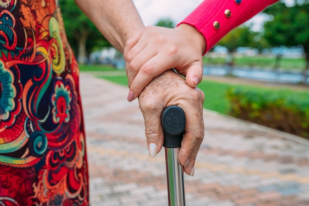 Les mains secourables pour le bâton de marche femme âgée soins à domicile dans un parc en plein air.