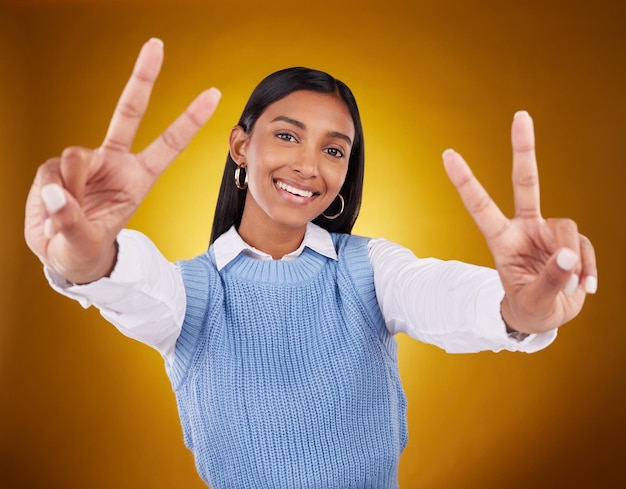 Mains signe de paix et portrait d'une femme indienne en studio pour le bonheur confiant et sourire sur fond marron Mode de maquette d'Emoji et fille avec geste de la main avec des cosmétiques de beauté et du style