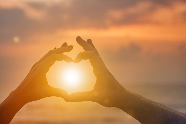 Les mains silhouette de la femme et de l'homme sont en forme de coeur avec le coucher du soleil à travers la main