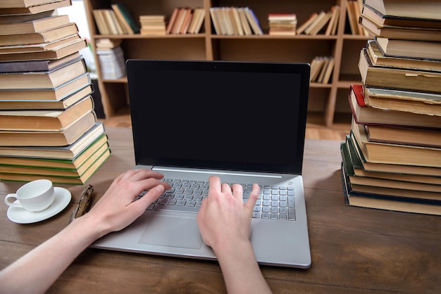 Les mains sont sur l'ordinateur portable dans la bibliothèque sur la table avec de nombreux livres et une tasse de café