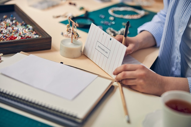 Mains d'un spécialiste des bijoux utilisant un stylo et écrivant un message sur du papier de certificat