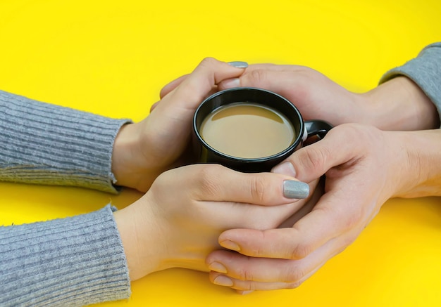 Les mains sur une surface jaune avec une tasse noire avec du café