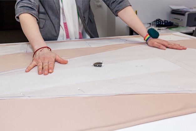 Mains de tailleur femelles avec le tissu, le modèle et l'aiguille dans l'atelier