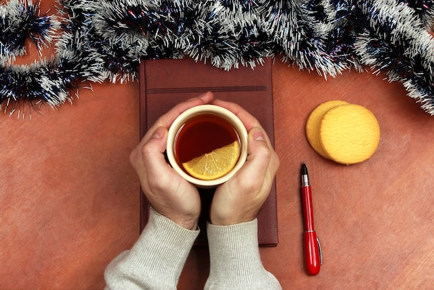 Les mains avec une tasse de thé sur la table de bureau avant Noël