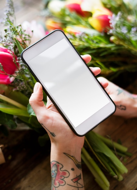 Mains tatouées avec téléphone portable avec écran blanc et bouquet de fleurs