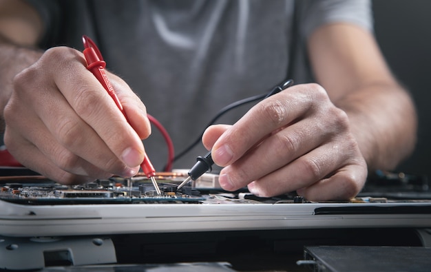 Mains de technicien vérifiant la carte mère avec le multimètre.