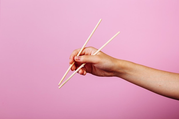 Mains tenant des baguettes. Isolé sur fond rose, la place pour la légende et le texte.