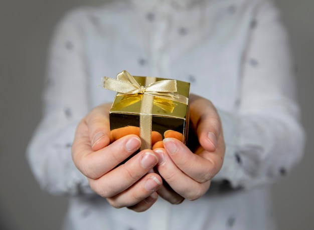 Mains tenant une boîte-cadeau en or isolée sur fond gris donnant un anniversaire de noël à la fête des mères o