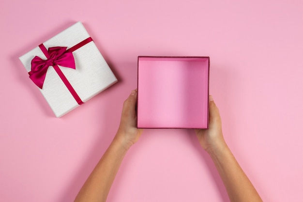 Mains tenant une boîte cadeau vide ouverte sur la vue de dessus de fond rose pastel