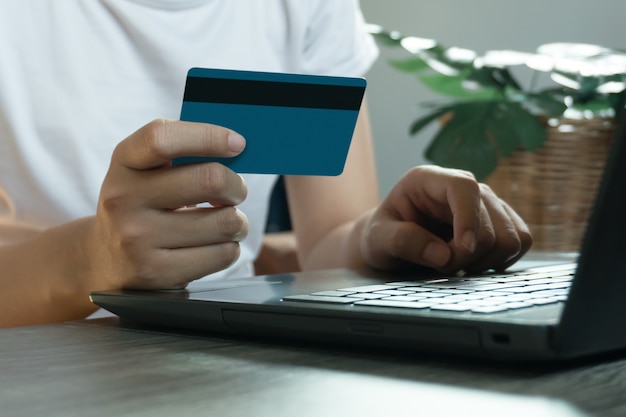 Mains tenant une carte de crédit et utilisant un ordinateur portable. Shopping en ligne. travail à domicile concept