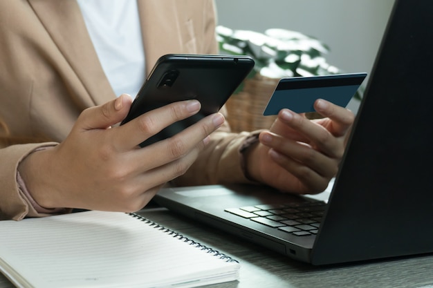 Mains tenant la carte de crédit et utilisant le téléphone et l'ordinateur portable. Achats en ligne concept de travail à domicile