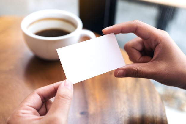 Mains tenant une carte de visite vide avec une tasse de café sur la table