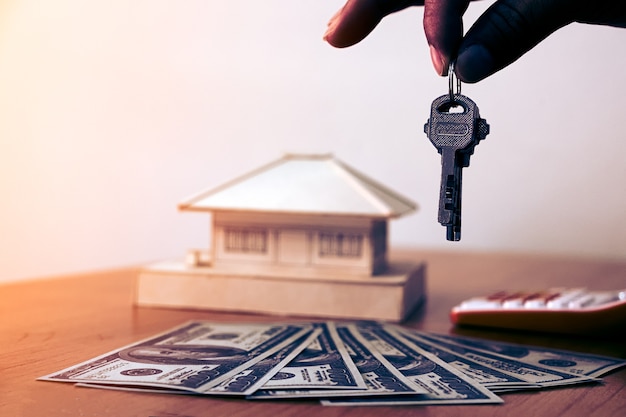 Mains tenant des clés de la maison avec de l&#39;argent et une petite maison sur une table en bois.