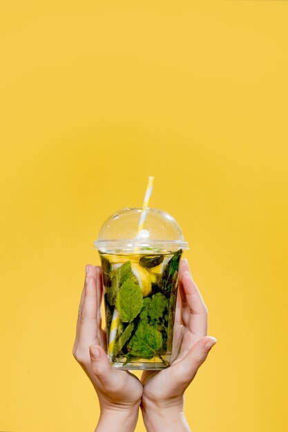 Mains tenant un cocktail mojito dans un ourson en plastique avec de la paille en plastique sur fond jaune