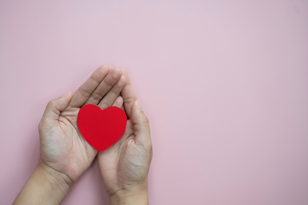 Mains tenant le coeur rouge sur l'espace de copie de fond rose pastel