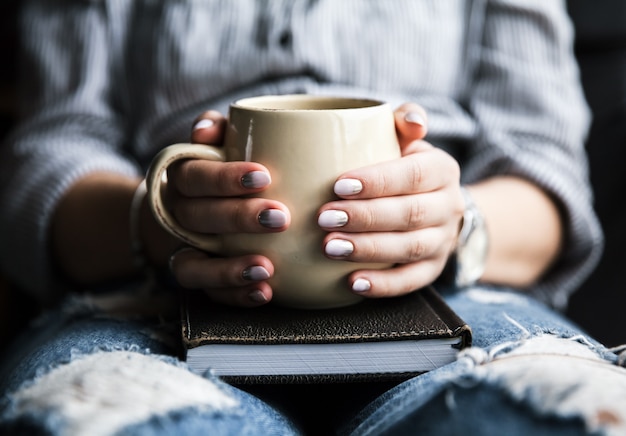 Mains tenant un livre avec une tasse de café