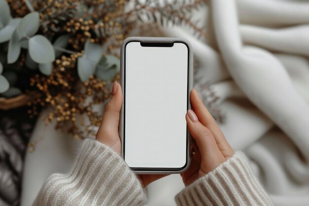 Des mains tenant une maquette de smartphone avec une couverture douce et des plantes décoratives en arrière-plan