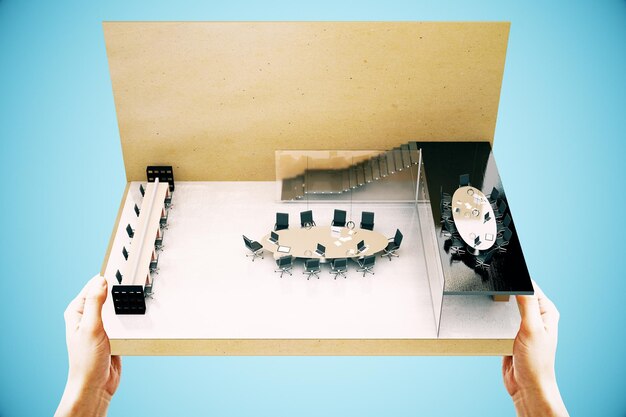 Des mains tenant une miniature de salle de conférence sur fond bleu Rendering 3D