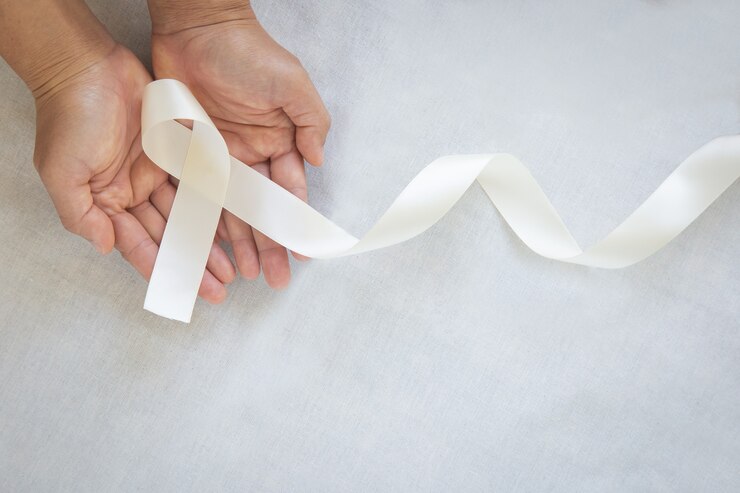 Mains tenant un noeud de ruban de perles blanches sur tissu blanc avec espace de copie. Sensibilisation au cancer du poumon, symbole du cancer du mésothéliome et du rétinoblastome.