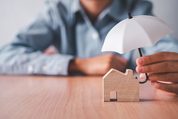 Mains tenant un parapluie sur une maison en bois. Concept d'assurance habitation, soins à domicile et sécurité.