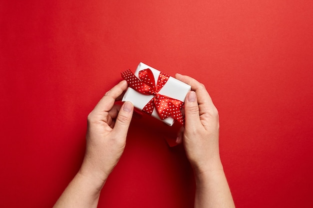 Mains tenant une petite boîte cadeau blanche avec ruban rouge