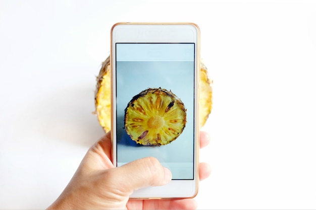 Photo mains tenant un smartphone mobile et prendre une photo d'un ananas