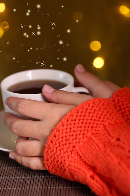 Mains tenant une tasse de boisson chaude, gros plan, sur une surface lumineuse