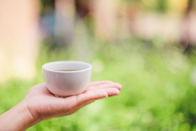 Mains tenant une tasse de thé sur fond vert bokeh