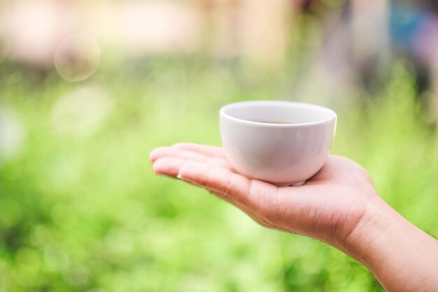 Mains tenant une tasse de thé sur fond vert bokeh