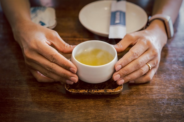 Mains tenant une tasse de thé vert chaud sur un plateau